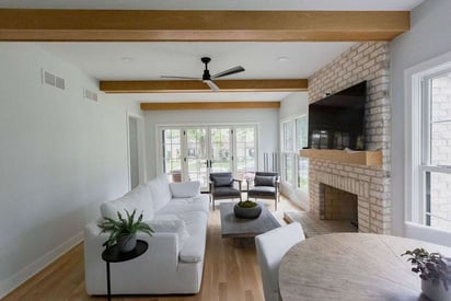 Living room with a wall mounted TV over a brick fireplace with exposed support beams