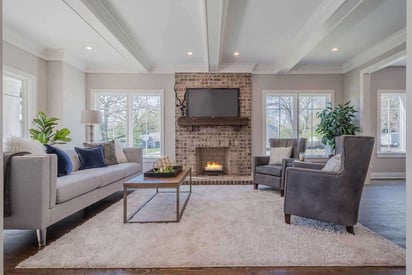 Living room with a brick fireplace on the wall with decorative rafters above the couch and chairs