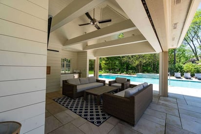 Pool house seating area with couches, a ceiling fan, and a wall mounted TV