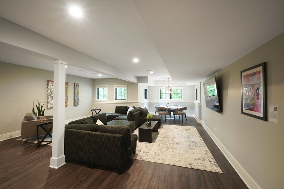 Basement remodeling project with luxury vinyl flooring, a support pillar in the middle, lots of furniture, and egress windows to let natural light pour into the space