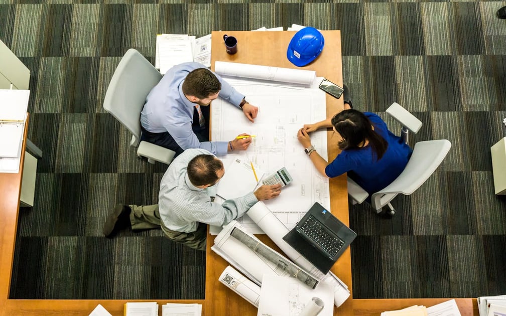 Architect, project manage, and interior designer collaborating around a table as they draw up a floor plan for a residential home remodeling project